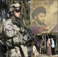 An Iraqi and a U.S. Army soldier stand guard next to a poster depicting radical Shiite cleric Muqtada al-Sadr during the reopening of a street in the Kazimiyah area of northern Baghdad , Iraq, Tuesday, Feb. 3, 2009. (AP)