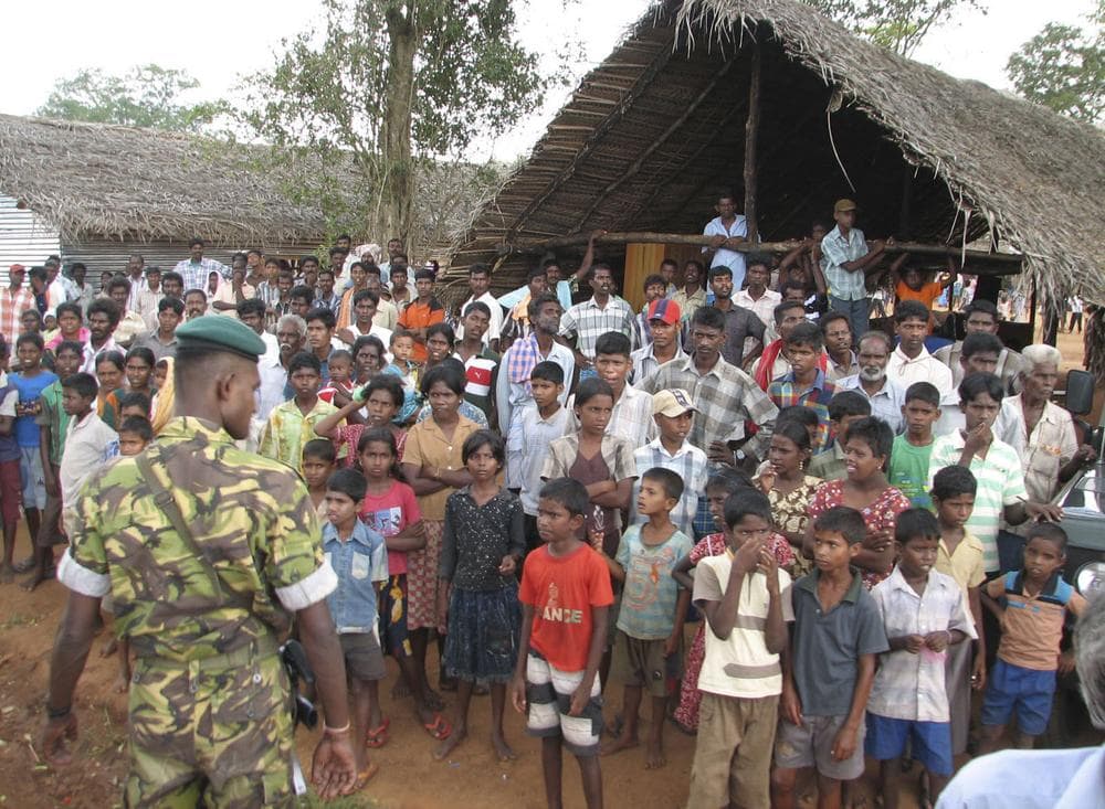 A Sri Lankan police commando stands guard as ethnic Tamils look on during the visit of French Foreign minister Bernard Kouchner, unseen, at the Manik Farm camp for internally displaced ethnic Tamils in Vavuniya, Sri Lanka, Wednesday, April 29, 2009. (AP)
