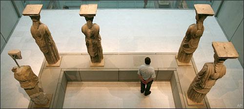 A visitor to the new Acropolis museum stands behind the Caryatids, female figures used instead of pillars, in Athens on Sunday, June 21, 2009. The empty space in front of the visitor denotes the absence of a Caryatid now on display at the British Museum in London. The Acropolis Museum opened its gates today to the first visitors who came to see the more than 4,000 exhibits on display, including those parts of Parthenon's marble frieze not held by the British Museum. (AP)