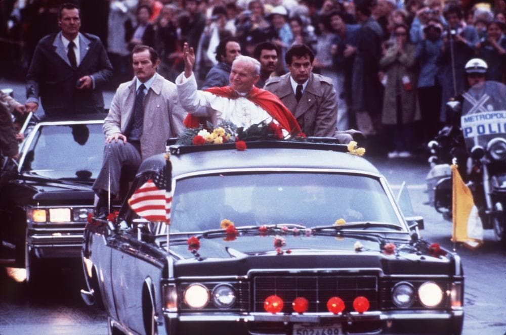 Pope John Paul II greets the crowd from his motorcade in the streets of Boston as Massachusetts State Police hold back crowds, Monday, Oct. 1, 1979. (AP Photo)