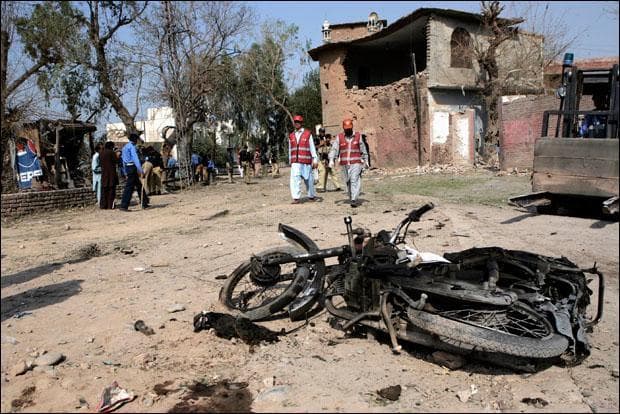 Pakistani officials walk near a wrecked motorcycle at the spot of a suicide bombing in Peshawar. (Mohammad Sajjad/AP)