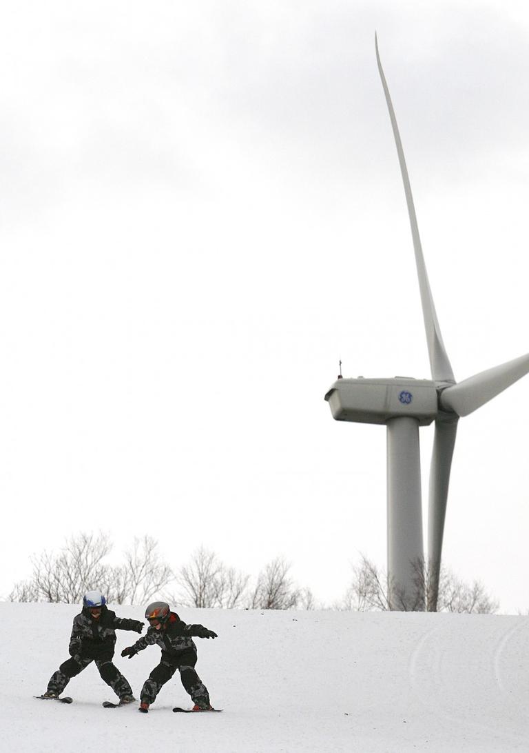 Ryan Dood, 8, left, reaches to help stabilize his younger brother, Evan, 7, as they ski down a Jiminy Peak Mountain Resort slope in front of the facility's 1.5-megawatt wind turbine in 2008. (AP)