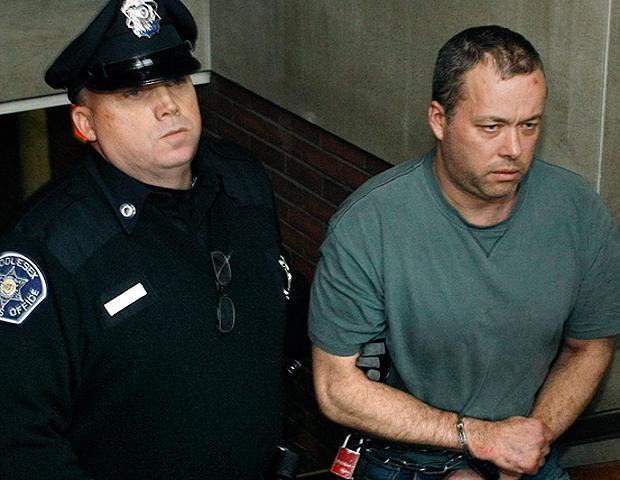 Mark Kerrigan, 45, the brother of figure skater Nancy Kerrigan, is led in handcuffs out of Woburn District Court after his arraignment Monday. He has been charged with assaulting their 70-year-old father, Daniel, who died over the weekend after a disturbance at the family's Stoneham home. (AP)