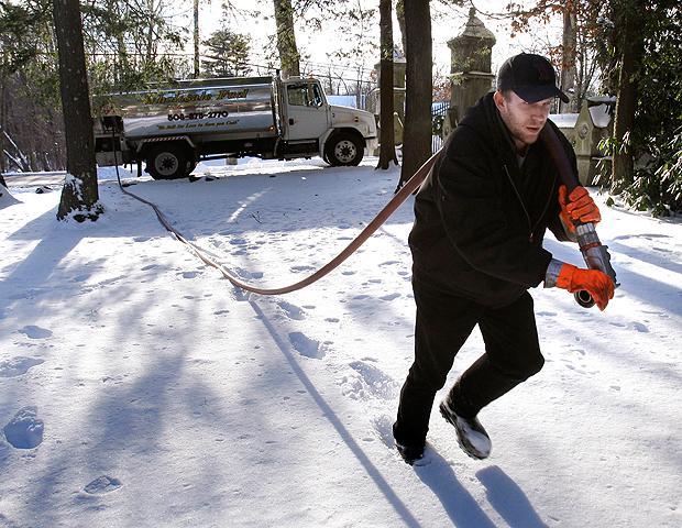 Jason Kilpatrick of Wholesale Fuel hauls a hose across a snow-covered yard while delivering home heating oil in Framingham on Jan 5. (AP)