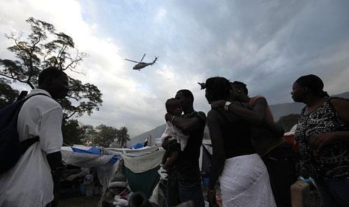 Haitians living in an improvised tent city watch a U.S. Navy helicopter on Monday, Jan. 25, 2010. (AP)