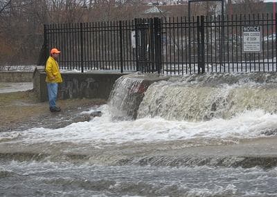 An official surveys flooding of the Charles River by the Moody Street dam in Waltham on Monday.  (Jack Lepiarz for WBUR)
