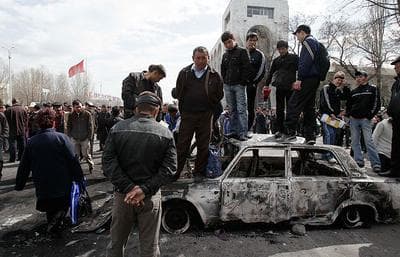 Men stand on a burned-out car in front of the Kyrgyz government headquarters in Bishkek, Kyrgyzstan on Thursday. (AP)