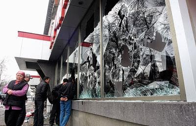 Kyrgyz people walk past windows of a shop broken by looters in Bishkek, Kyrgyzstan on Thursday. (AP)