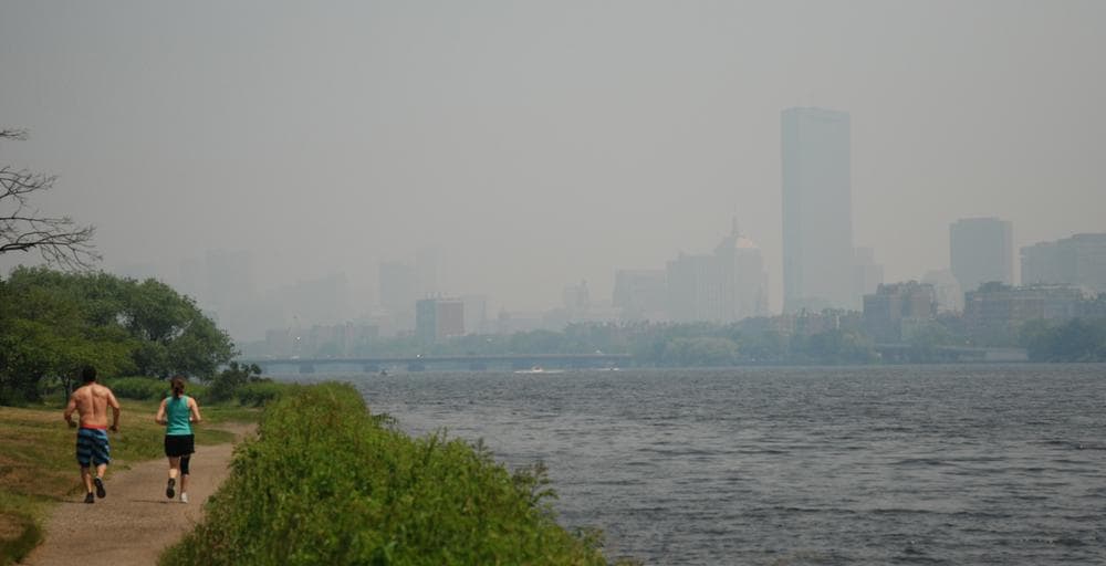 Joggers run along the Charles on Monday. Behind them, the Boston skyline is obscured by the smoky haze from wildfires in Canada. (Jess Bidgood for WBUR)