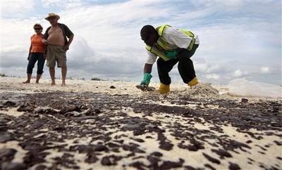 Tourists watch as Steve Gardner of Mobile scrapes oil from the sand along a 700-yard long strip of oil that washed up on the beach in Gulf Shores, Ala. (AP)