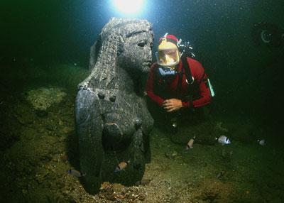 A diver is inspecting a Granite head emerging from the sediment at the Heracleion site. The head belongs to a statue of a Ptolemaic Queen dressed as the Goddess Isis. (Credit: Franck Goddio / Hilti Foundation, Photo: Christoph Gerigk)