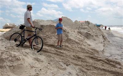 A father and son watch the cleanup of tar balls by oil cleanup workers in Dauphin Island, Ala., on Sunday, July 4th, 2010. City officials canceled their Fourth of July festivities because of the Deepwater Horizon oil spill. (AP)