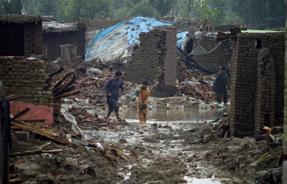 Flood-affected people walk past the rubble of collapsed houses near Nowshera, Pakistan, on Aug. 8, 2010. (AP) 
