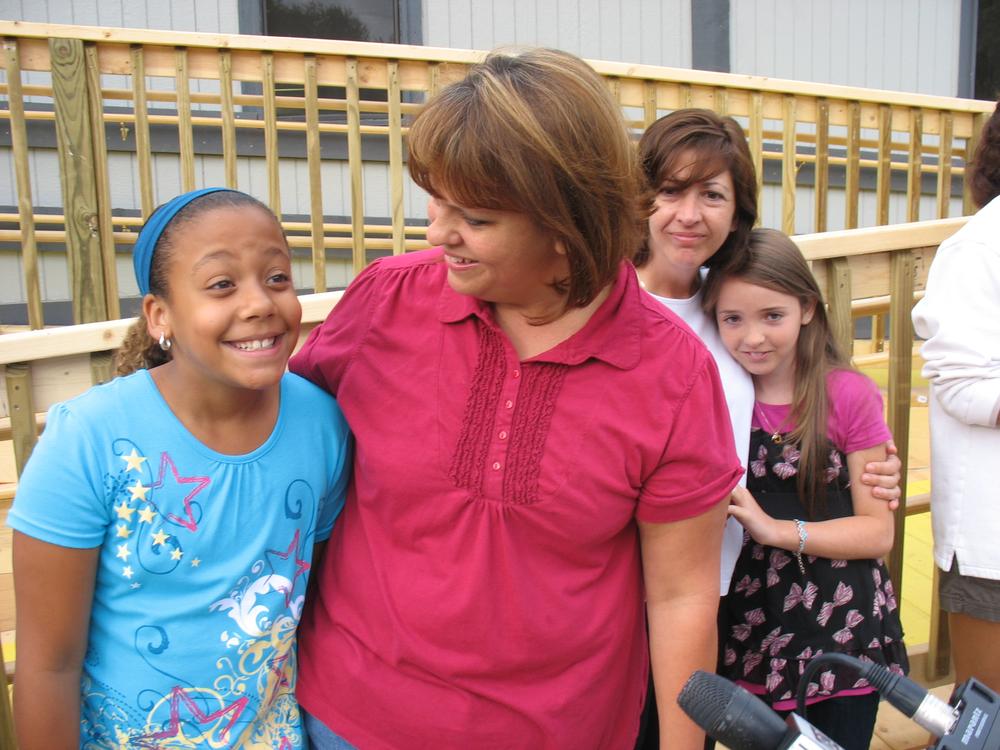 9 year old Alexis Exama can't contain her excitment that the charter school is open.  Her mother Ruthie Exama was faught hard to get the school going.  Behind them are Jennifer Schulman and her daughter Joscelyn, going into the 5th grade. (Photo by WBUR)