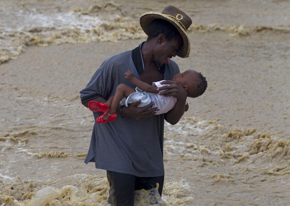 A man carries a child while wading across a flooded street during the passing of Hurricane Tomas in Leogane, Haiti, Friday. (AP Photo/Ramon Espinosa)
