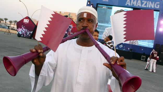 A Qatari man waves the national flag as he blows vuvuzelas at Doha's traditional souk. FIFA announced Thursday that Qatar won its bid to host the 2022 World Cup. (AP)