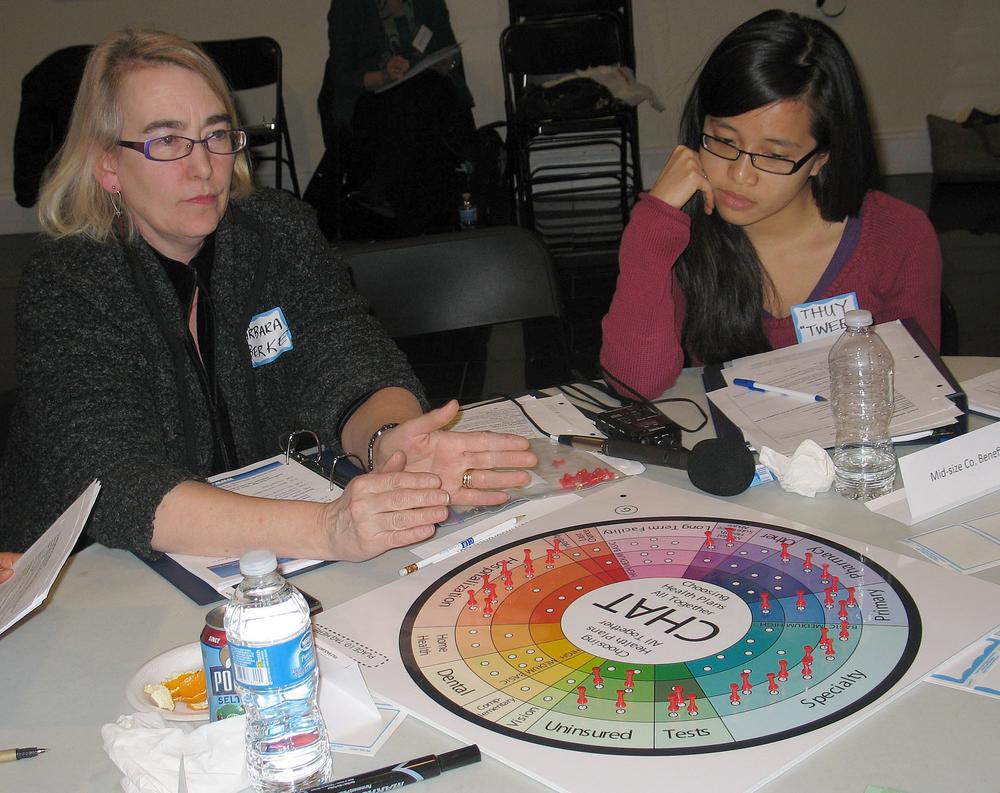 Barbara Berke, left, with the Greater Boston Interfaith Organization, takes Thuytien Le and other members through a game of choosing priorities in health care. (Martha Bebinger/WBUR)