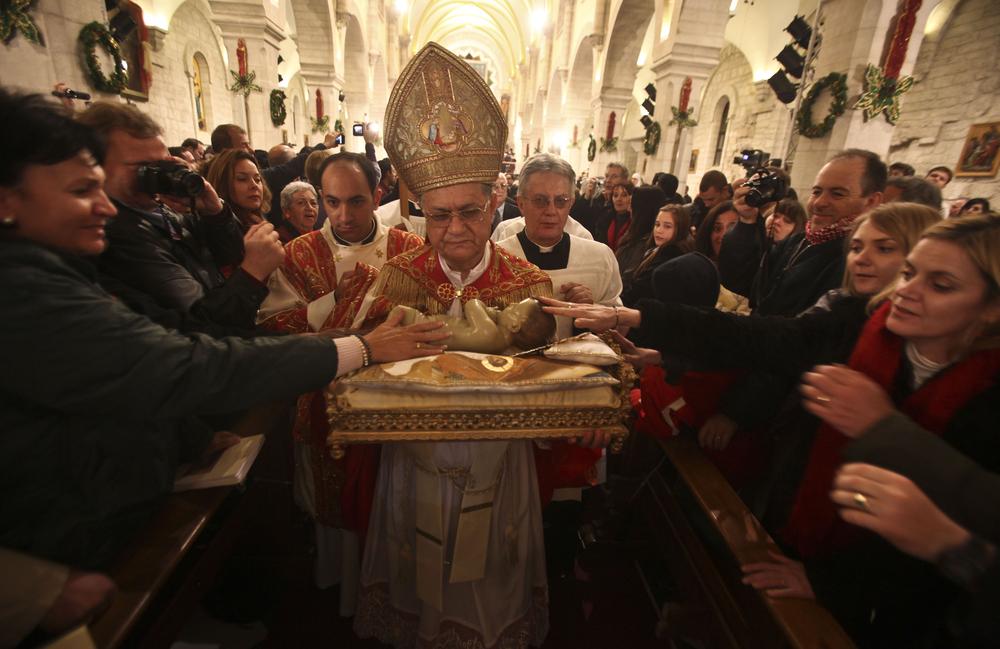 Latin Patriarch of Jerusalem Fouad Twal carries the statuette of baby Jesus during the midnight Mass ceremony which marks the beginning of Christmas Day at the Church of the Nativity in the West Bank town of Bethlehem early Saturday. (AP Photo//Fadi Arouri, Pool)