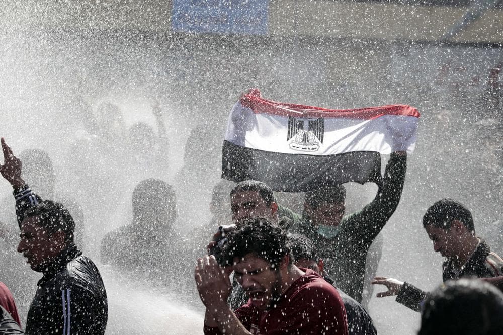 An Egyptian protester flashes Egypt's flag as anti-riot policemen use water canon against protesters in Cairo, Egypt. (AP)