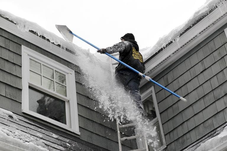Andrew Santino, of Santino's Roofing and Asphault, uses a rake to clear snow from a residential roof in Andover on Wednesday. A massive snowstorm enveloping much of the nation has brought building roofs to the breaking point in a winter that has already delivered more snow than many cities typically see in a whole season. (AP)