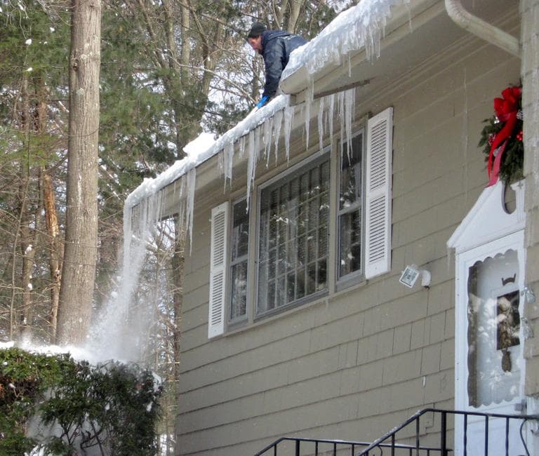 One roofer clears out an ice dam that has formed atop a home in Acton. (David Boeri/WBUR)