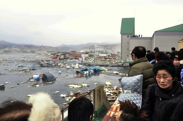 People watch the aftermath of tsunami tidal waves covering a port at Kesennuma in northern Japan, Friday. (AP/Keichi Nakane, The Yomiuri Shimbun) 