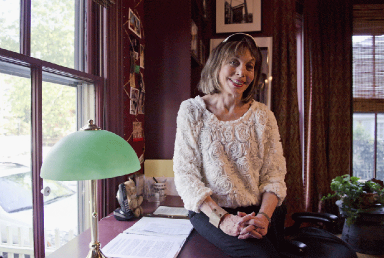 Joan Parker sitting on her late husband's desk. Behind Joan is a teddy bear that her husband, author Robert Parker, had since childhood. (Anna Miller/Here &amp; Now)