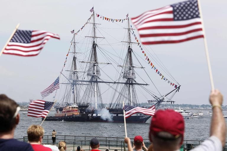 Spectators wave flags as the USS Constitution fires its cannons off Castle Island in Boston on its annual Fourth of July turn around in Boston Harbor on Monday. (AP)