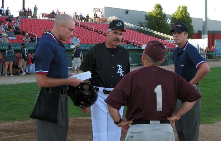 Bill Buckner, in black, speaks with umpires and the opposing manager before a recent Brockton Rox game. (Anthony Brooks/WBUR)