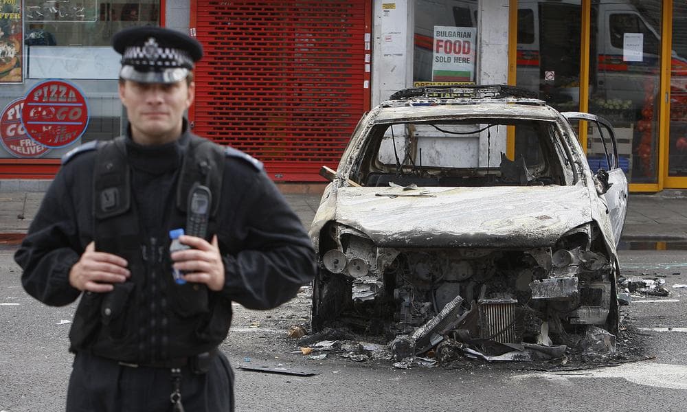 A police officer stands guard in front of a burned police car in Tottenham, north London. (AP)
