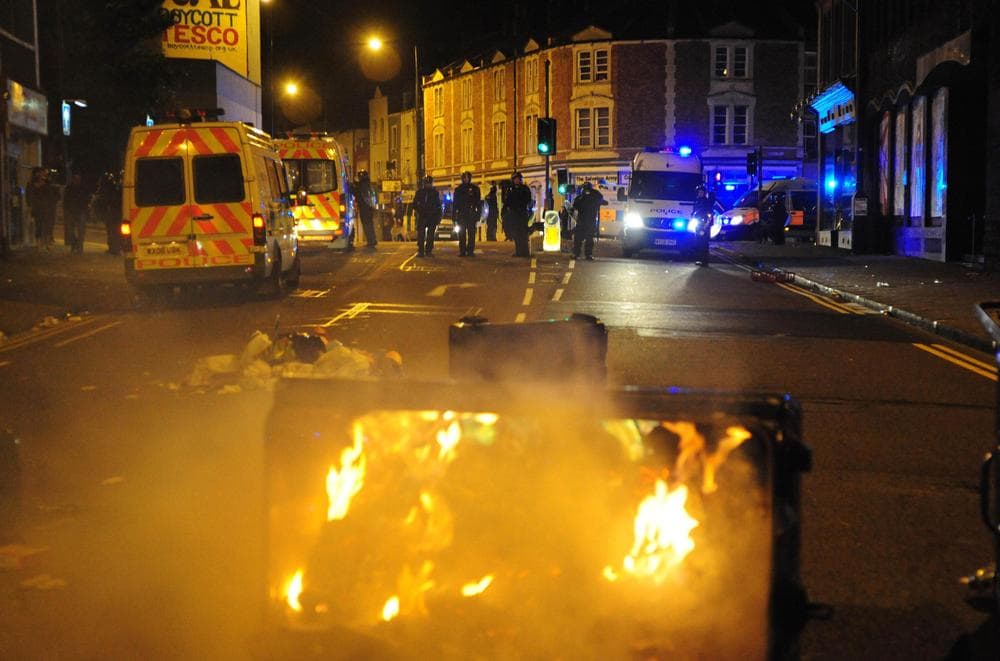 A trash bin burns as police officers patrol the streets in Bristol, England. (AP)