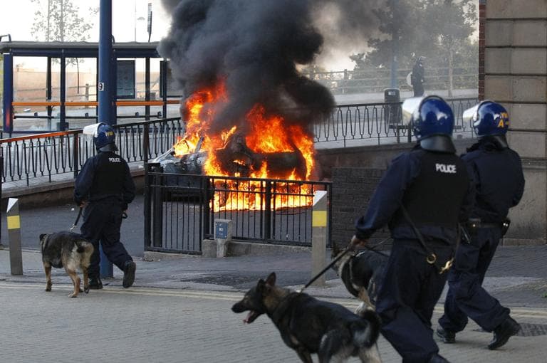 A Police dog and its handler walk past a burning car during the second night of civil disturbances in central Birmingham, England, Tuesday, Aug. 9, 2011. (AP)