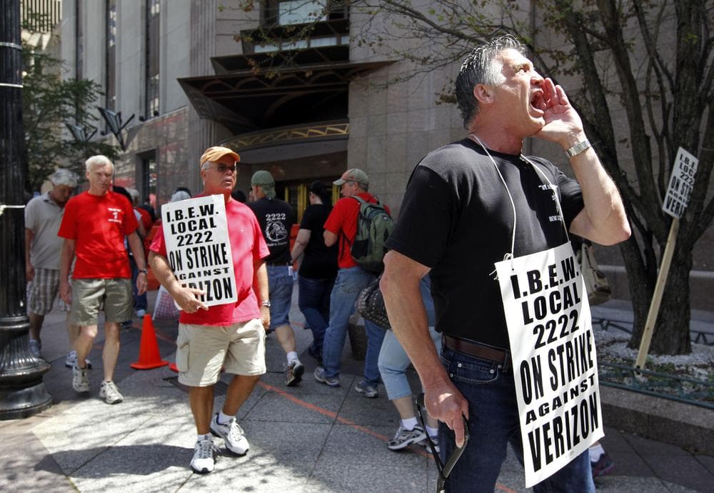 Verizon worker Steven Simard, of Danvers, right, holds a placard and chants slogans from a picket line outside a Verizon office in Boston Aug. 12. (AP)