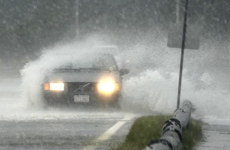 A passenger vehicle is buffeted by strong winds and ocean spray from tropical storm Irene while driving along a coastal road in Oak Bluffs, Sunday. (AP)