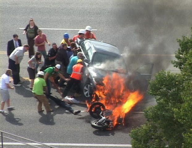 A group of people tilt a burning BMW up to free Brandon Wright, on his back on the ground, who was pinned underneath after he collided with the car while riding his motorcycle on U.S. 89 in Logan, Utah. Wright survived. (AP)
