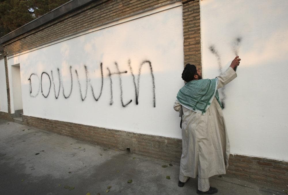 An Iranian cleric spray paints graffiti on the inside wall of the British Embassy while demonstrators stormed the embassy, in Tehran, Iran. (AP)