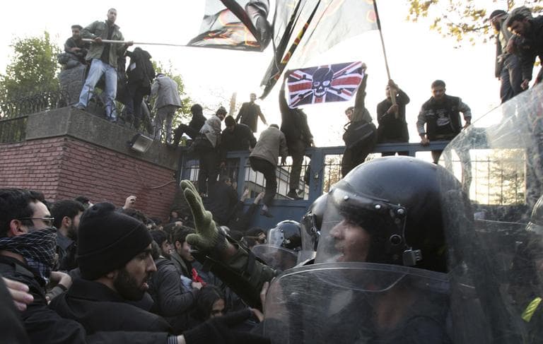 Iranian police officers prevent further protesters from entering the British Embassy, as others stand on the gates holding a satirized British flag and Islamic flags, in Tehran, Iran, Tuesday, Nov. 29, 2011. (AP)
