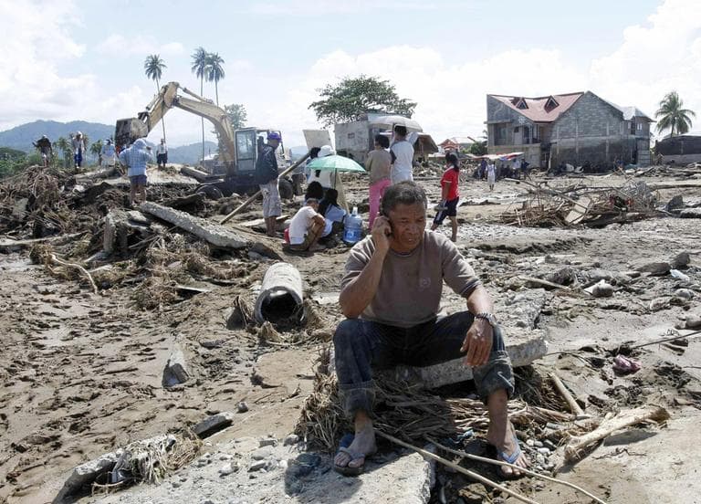 Cristio Tingson, foreground, talks on his cell phone as workers use a backhoe to search for victims of his buried house Sunday, Dec. 18, at Iligan city in southern Philippines. (AP)