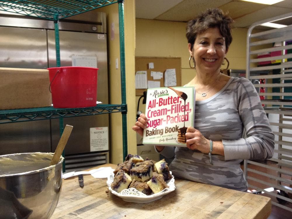 Judy Rosenberg, owner of Rosie's Bakery, at the original Rosie's in Inman Square with her new cookbook and a plate of her fresh Blueberry-Muffin Breakfast Cake. (Adam Ragusea/WBUR)