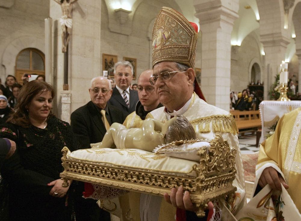 Latin Patriarch of Jerusalem Fouad Twal  carries the statuette of baby Jesus during the Christmas midnight Mass at the Church of the Nativity, traditionally believed to be the birthplace of Jesus Christ, in the West Bank town of Bethlehem early Sunday. (AP)