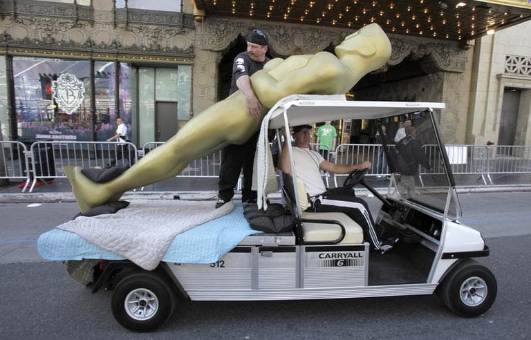 With B.J. Nicodemus driving the golf cart, Shawn Schull hangs onto a large Oscar statue outside the Kodak Theater in Los Angeles on Friday, Feb. 20, 2009. (AP)