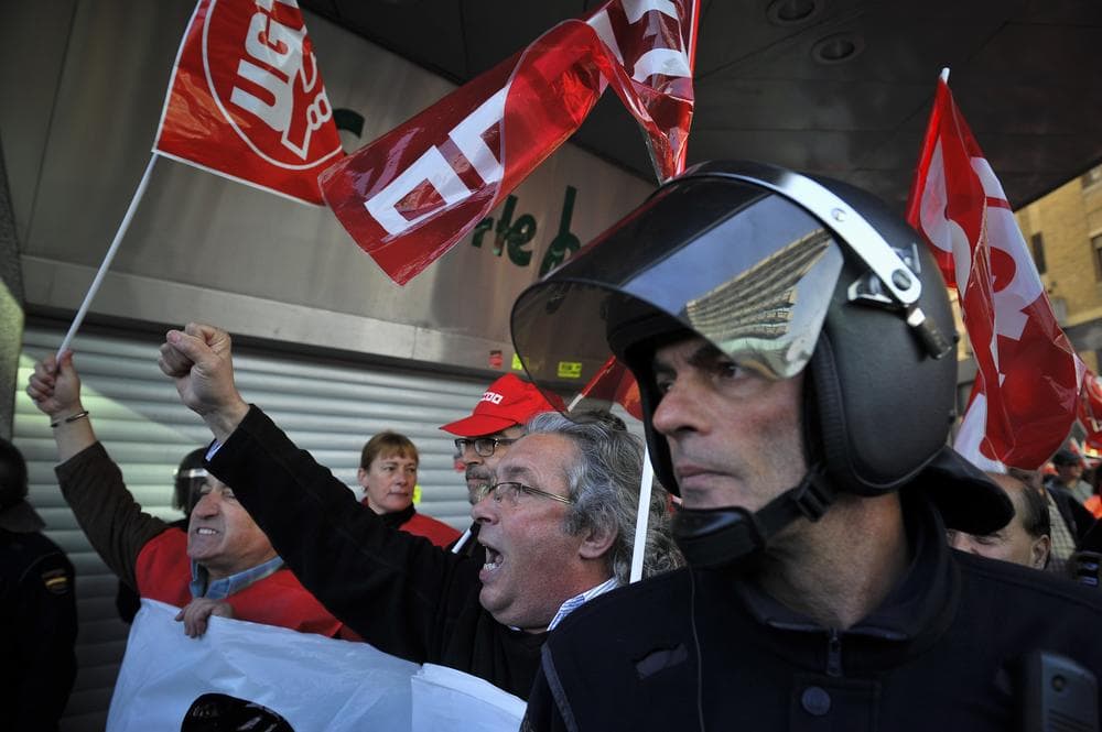 Demonstrators march with union flags as a police officer stand beside them during a general strike in Pamplona, northern Spain, Thursday. (AP)