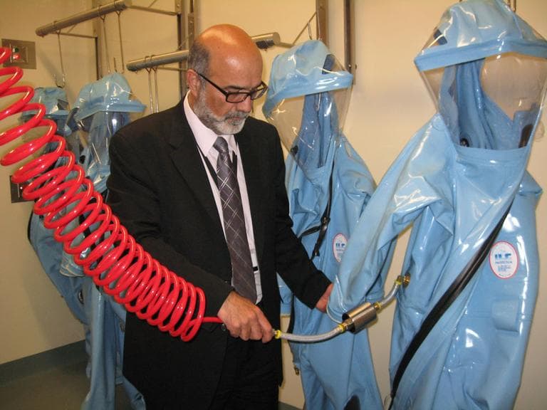 Ara Tahmassian, NEIDL associate director and associate vice president for research compliance at Boston University, demonstrates how biosafety level 4 researchers will hook HEPA air hoses to their protective suits. (Lynn Jolicoeur for WBUR)