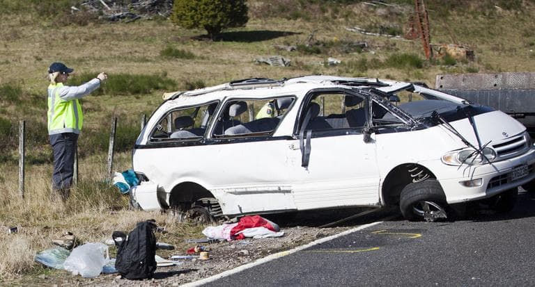 A policeman examines the scene of a minivan crash near Turangi, New Zealand. that killed three Boston University Students on May 12, 2012. (AP)