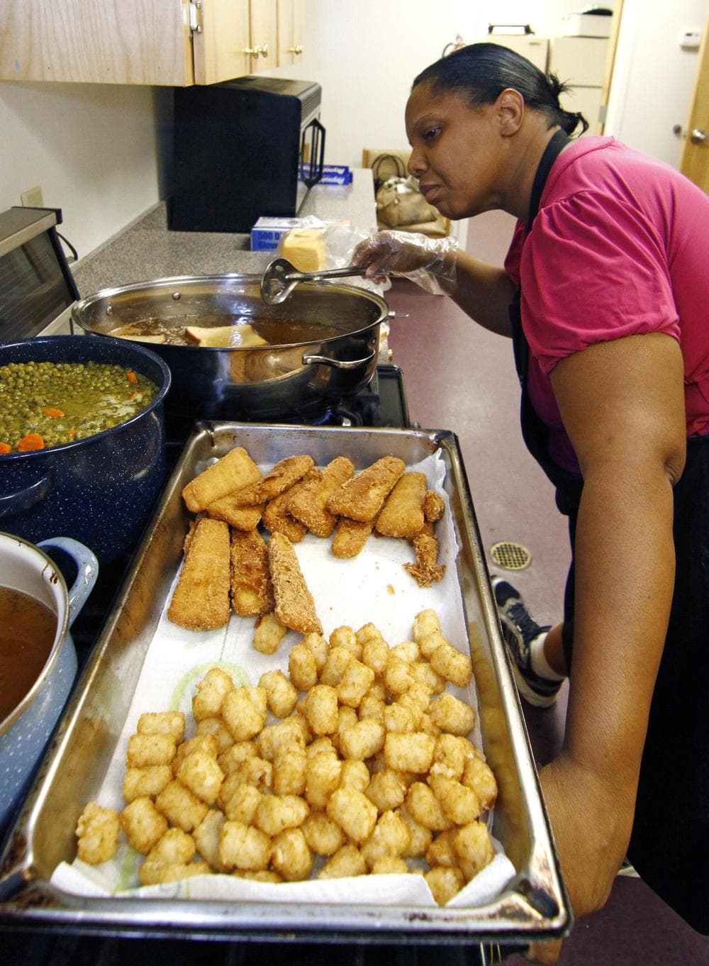 Earnestine Nelson, chief cook for the Alpha and Omega Church's free summer meals program for children and teens, checks the progress of her peas and carrots while frying fish fillets and tater tots for lunch in Jackson, Miss. (AP)