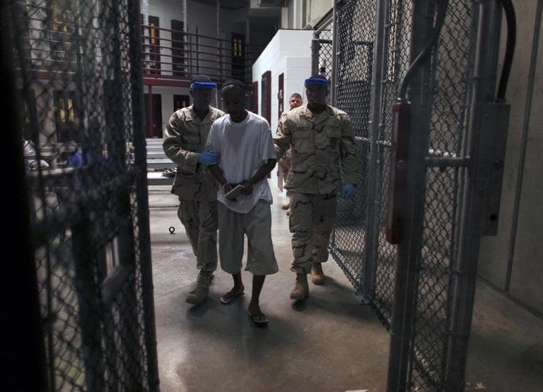 A Guantanamo detainee carries a workbook as he is escorted by guards after the detainee attended a class in "Life Skills" at Guantanamo Bay detention facility in March 2010. (AP/Brennan Linsley)