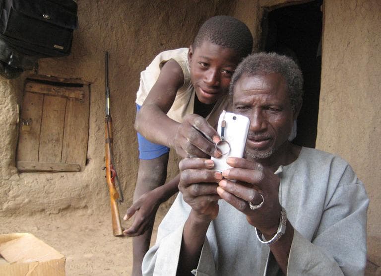 An unidentified boy helps Alaburu Maiga use his cell phone in the village of Gono, Mali. Across the developing world, cell phones are multiplying. (AP/Heidi Vogt)