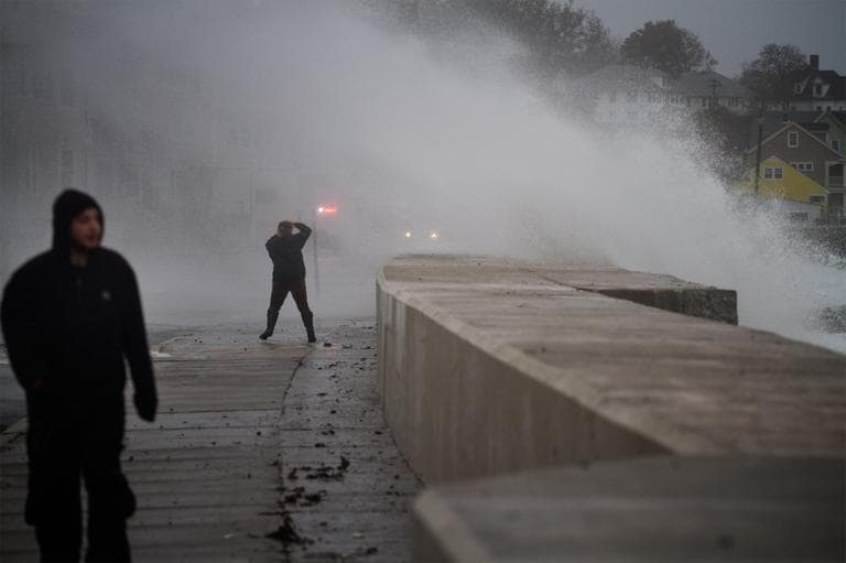 A bystander covers up from being hit with wind and a crashing wave on Winthrop beach. (Jesse Costa/WBUR)