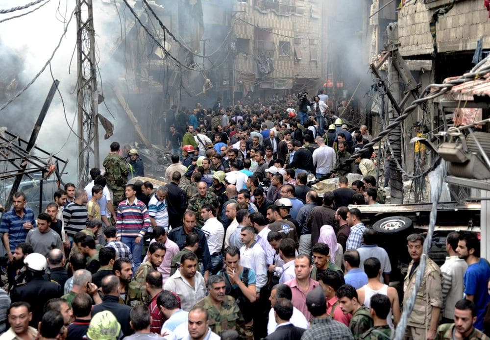 This photo released by the Syrian official news agency SANA, shows Syrians standing at the scene after a blast occurred in the Mazzeh al-Jabal district of the Syrian capital Damascus on Monday. State-run television said several people were killed and injured, among them children. (SANA/AP)