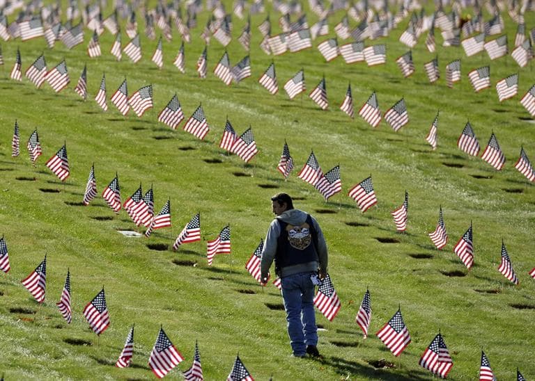 Jason Machado, of Fairhaven, walks among U.S. flags at the graves of deceased veterans at the National Cemetery in Bourne Saturday. (Gretchen Ertl/AP)